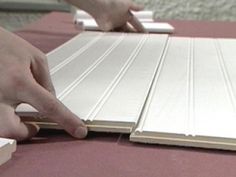 two hands are pointing at the top of a table with white tiles on it and one hand is touching the edge of the board