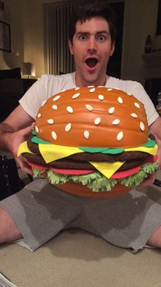 a man sitting on the floor holding a giant hamburger