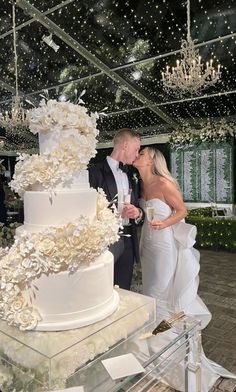 a bride and groom kissing in front of a wedding cake with white flowers on it