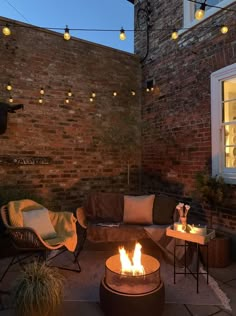 a fire pit sitting in the middle of a patio next to a brick wall with lights on it