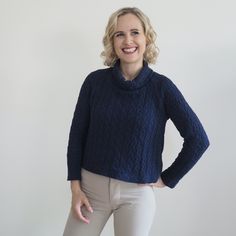 a woman wearing a blue sweater and white pants smiles while standing in front of a white wall