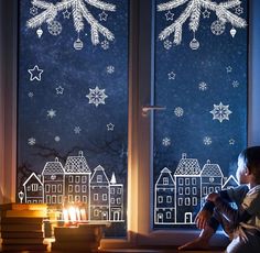 a young boy sitting on a window sill in front of a christmas scene with snowflakes