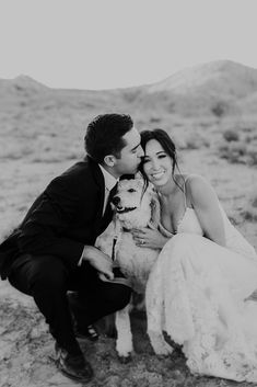 a bride and groom pose with their dog in the desert