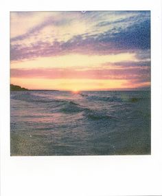 a polaroid photo of the sun setting over the ocean with waves crashing in front of it