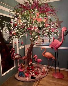 pink flamingos are sitting under a christmas tree with lights and ornaments on it's branches