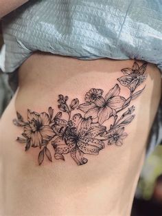 a woman's stomach with flowers and leaves tattoo on her side ribcage