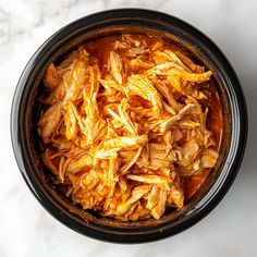 a bowl filled with shredded chicken sitting on top of a white marble countertop next to a knife and fork