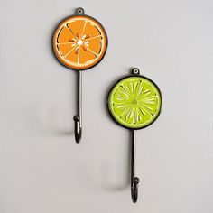 two orange slices are hanging from hooks on a white wall, one is green and the other has an orange slice painted on it