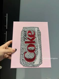 a hand holding up a pink card with the word coke on it in red and silver sequins