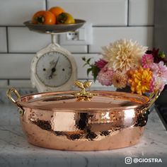 a large copper pot sitting on top of a counter next to flowers and an alarm clock