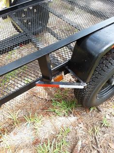 a black trailer is parked in the grass and has two wheels attached to it's sides