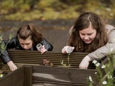 two girls looking at plants in a wooden box