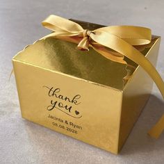 a gold gift box with a ribbon tied around the top and thank you written on it