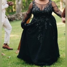 a woman in a black dress is standing on the grass with other people behind her