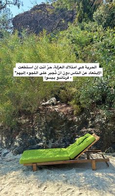 a green chaise lounger sitting on top of a sandy beach next to trees