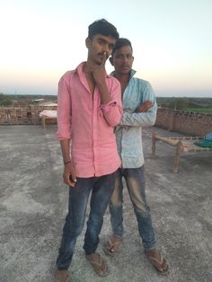 two young men standing next to each other on top of a cement ground with their arms crossed