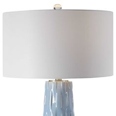 a table lamp with a white shade on the base and a light blue vase underneath it