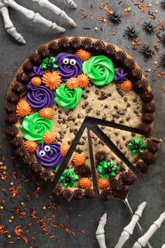 a cake decorated with halloween decorations and sprinkles on a gray table next to skeleton bones