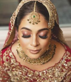 a woman in a red and gold bridal outfit with jewelry on her head, looking at the camera