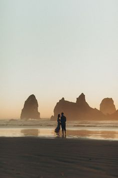 two people standing on the beach at sunset with their arms around each other as they kiss