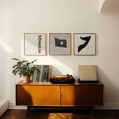 three framed pictures hang on the wall above a wooden cabinet with records and a record player