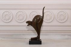 a bronze sculpture of a cat on a black stand in front of a white wall