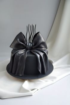 a black hat with a bow on it and forks sticking out of the top, sitting on a white cloth