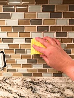 a hand with a yellow cloth on top of a counter next to a soap dispenser