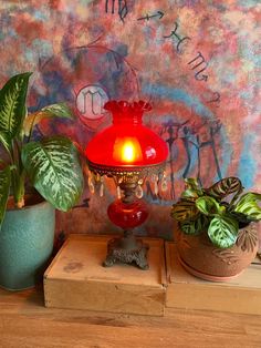 a red lamp sitting on top of a wooden table next to two potted plants