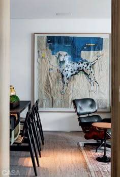 a black chair sitting next to a wooden table in front of a painting on the wall