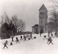 a group of people riding skis down a snow covered slope next to a tall building