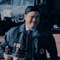 a man holding two cups in his hands and smiling at the camera while standing next to a truck