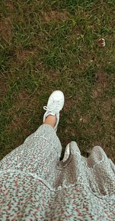 a person wearing white tennis shoes standing in the grass