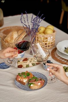 two people are toasting with wine at a table full of food and breads