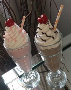 two ice cream sundaes with cherries and whipped cream on top sitting on a glass table