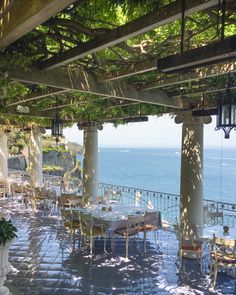 an outdoor dining area overlooking the ocean with tables and chairs set up for dinner under pergolated roof