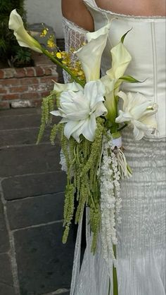 a woman in a wedding dress holding a bouquet of white flowers and greenery on her arm