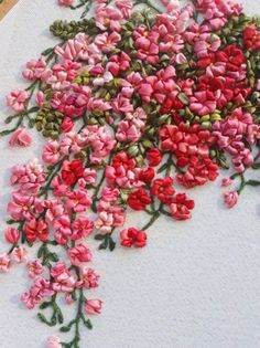 a close up of a cross stitch with pink flowers on white fabric and green stems