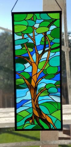 a stained glass window with a tree in the center and blue sky behind it, hanging on a chain