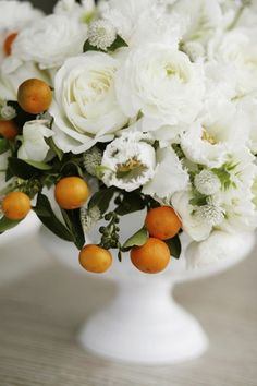 an arrangement of white flowers and oranges in a vase