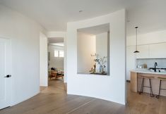 an empty kitchen with white walls and wood flooring is seen from the living room