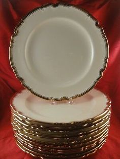 a stack of white and gold plates sitting on top of each other in front of a red cloth