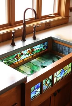 a stained glass sink in a kitchen with wooden cabinets and windows above it, along with two faucets