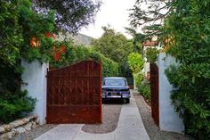 a car is parked in front of a gated driveway with trees and bushes on either side