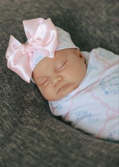 a baby wearing a pink bow laying on top of a bed next to a pillow