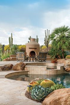 an outdoor fireplace in the middle of a pool surrounded by rocks and cactus plants with chairs around it