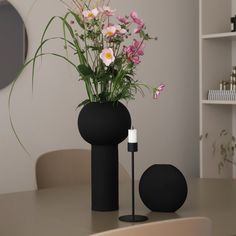 a black vase with flowers in it sitting on a table next to a white candle