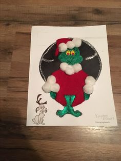 a paper cut out of a green and red christmas character on top of a wooden table