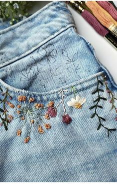 a pair of jeans with embroidered flowers on the side and some yarn next to it