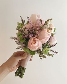 a hand holding a bouquet of flowers on a white background with pink and green foliage